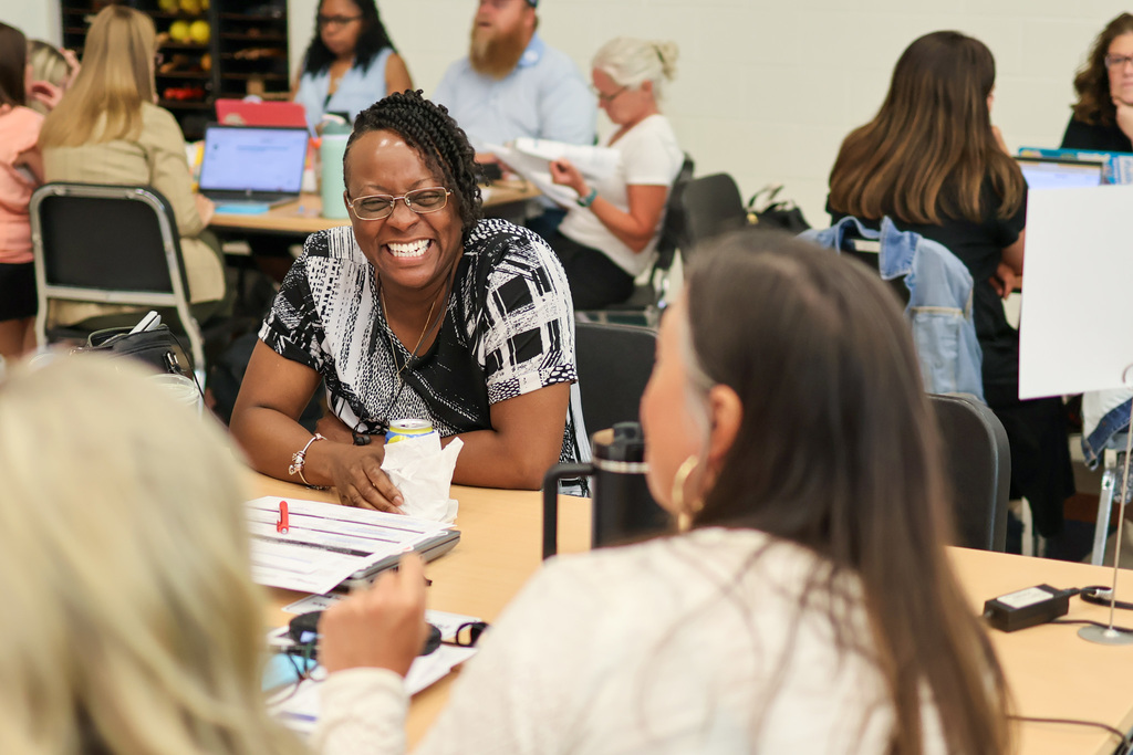 a woman laughs at a table in a room of people