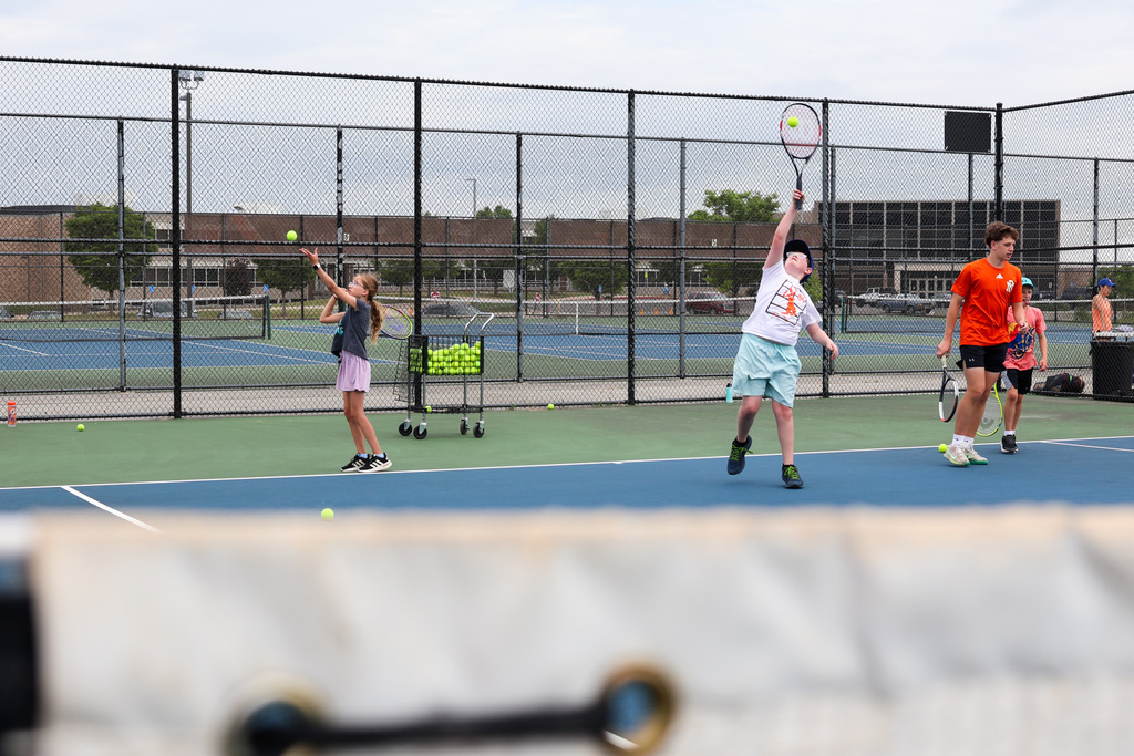 two students serve tennis balls across a tennis court
