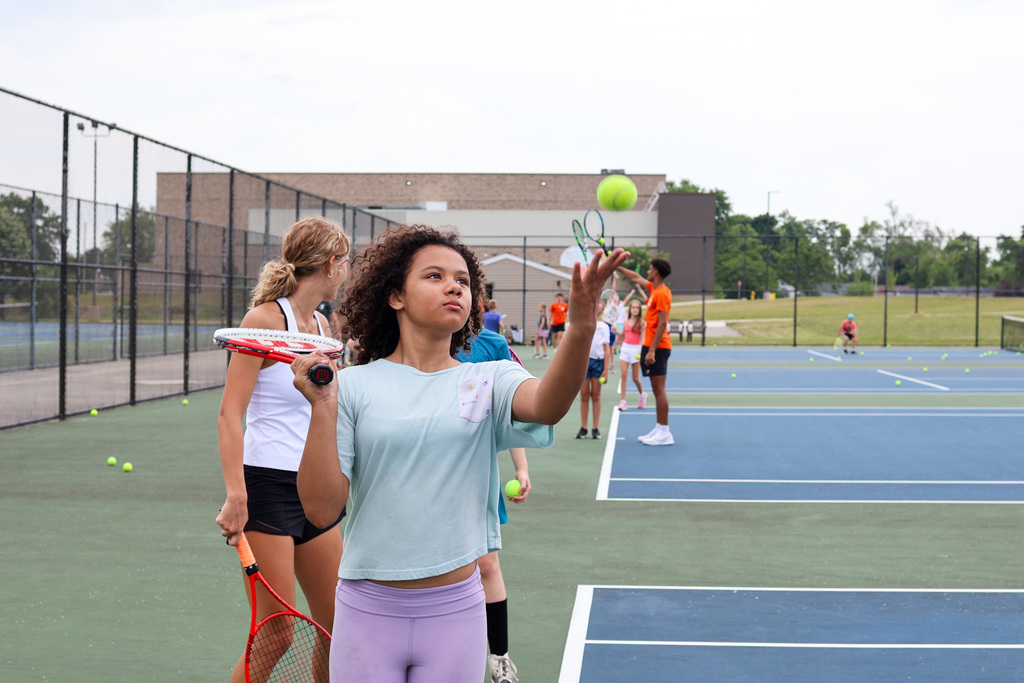 a girl throws a tennis ball in the air to serve