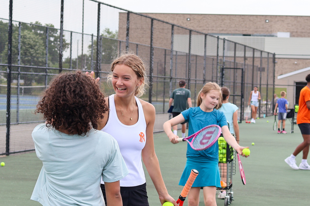 a girl smiles at another girl on a tennis court
