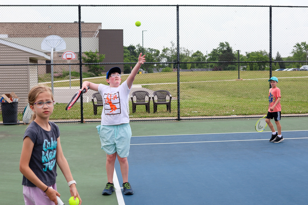 a boy serves a tennis ball