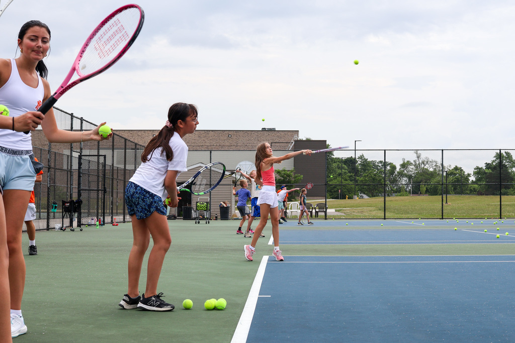 a girl serves a tennis ball surrounded by others