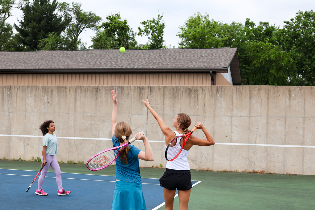 two girls serve a tennis ball