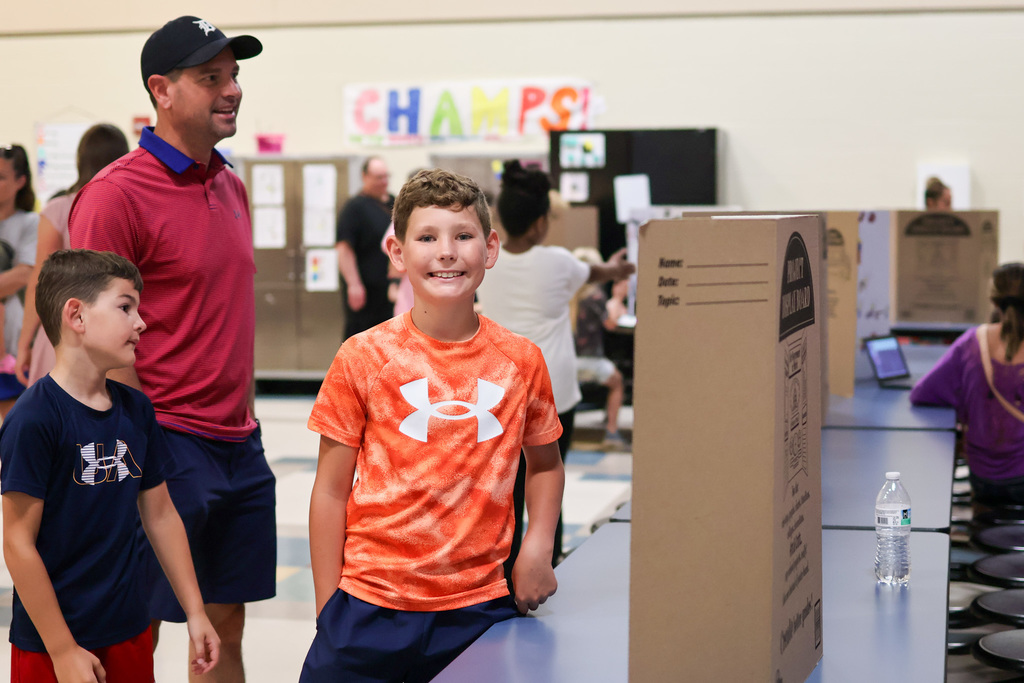 a boy smiles for a photo standing next to his presentation