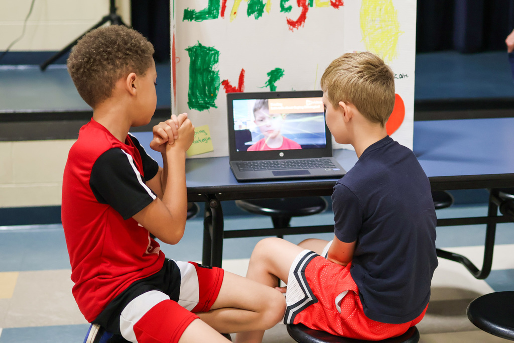 two boys sitting at cafeteria tables watch a podcast on a laptop