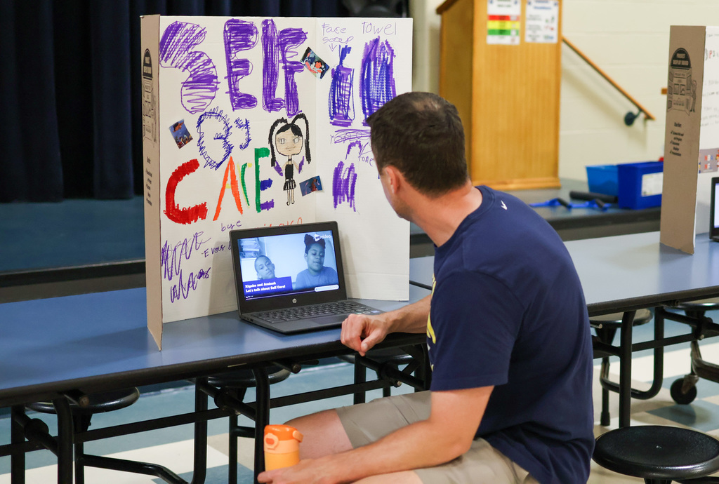 a teacher sits and watches a podcast on a laptop in a school cafeteria