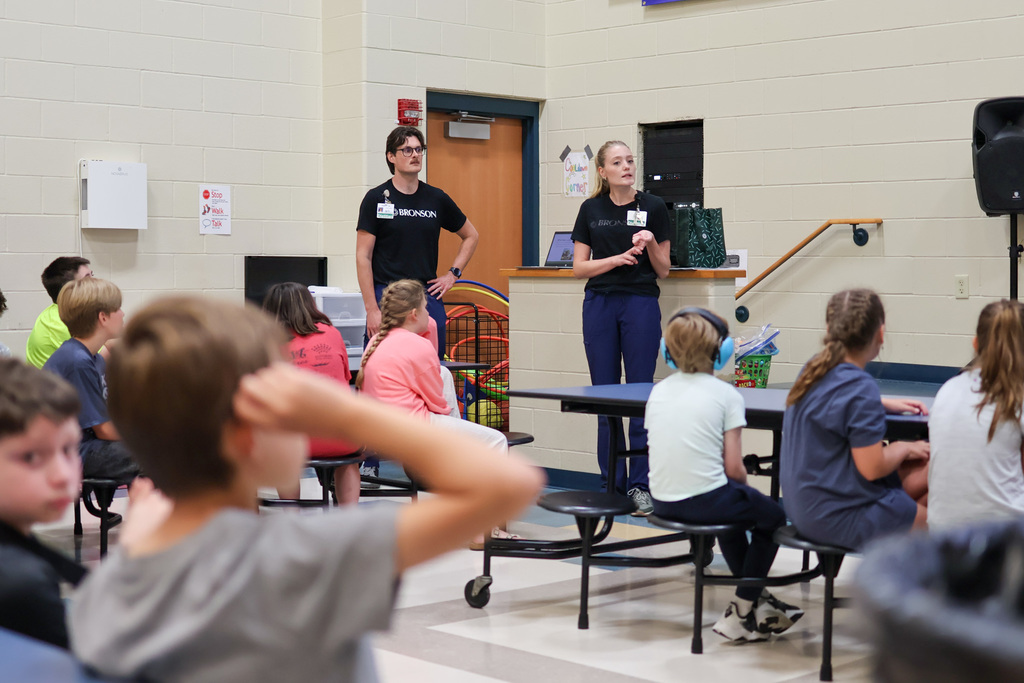 a woman speaks to students inside a school cafeteria