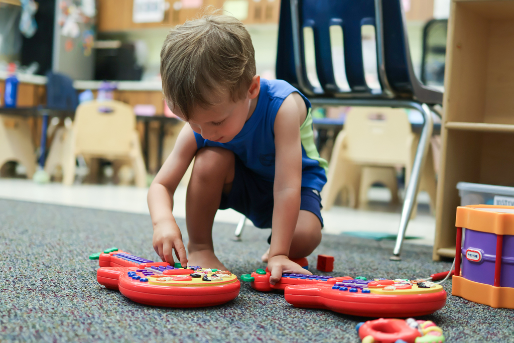 a young boy plays with a toy guitar inside a classroom