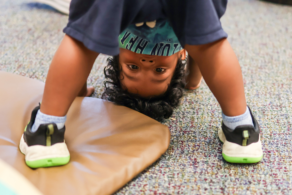 a young boy peers at the camera from between his legs