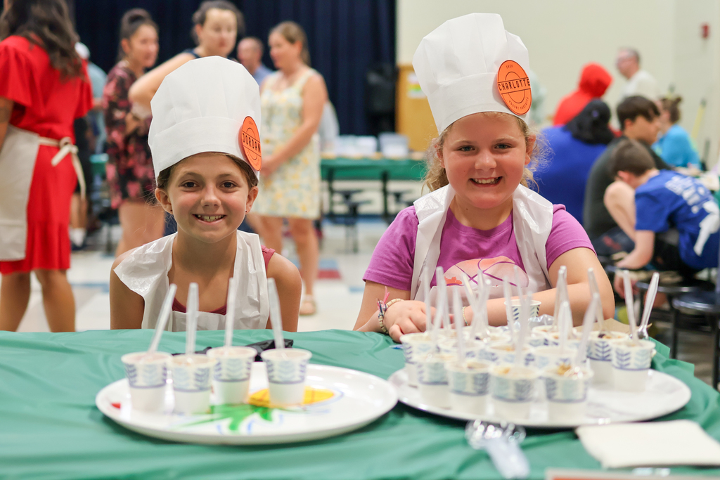 two girls in chef hats smile at the camera