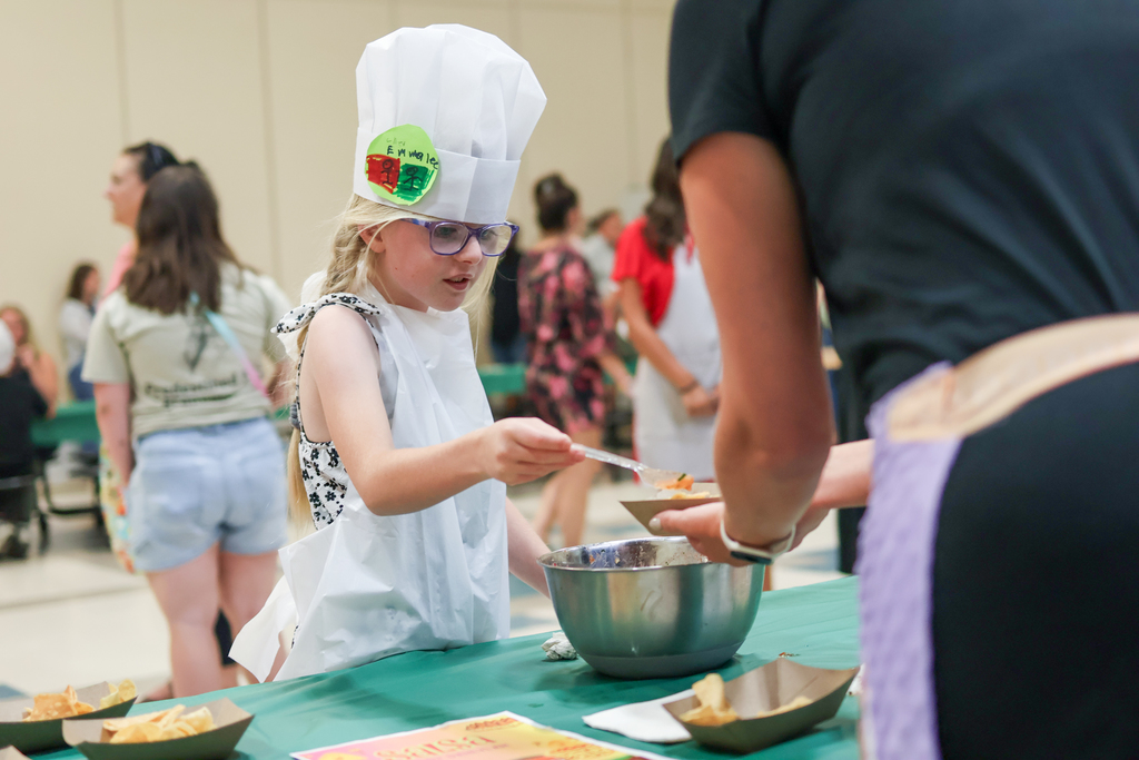 a girl in a chef hat gives food to a parent