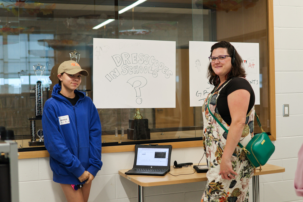 a girl poses for a photo next to her poster while a listener stands nearby