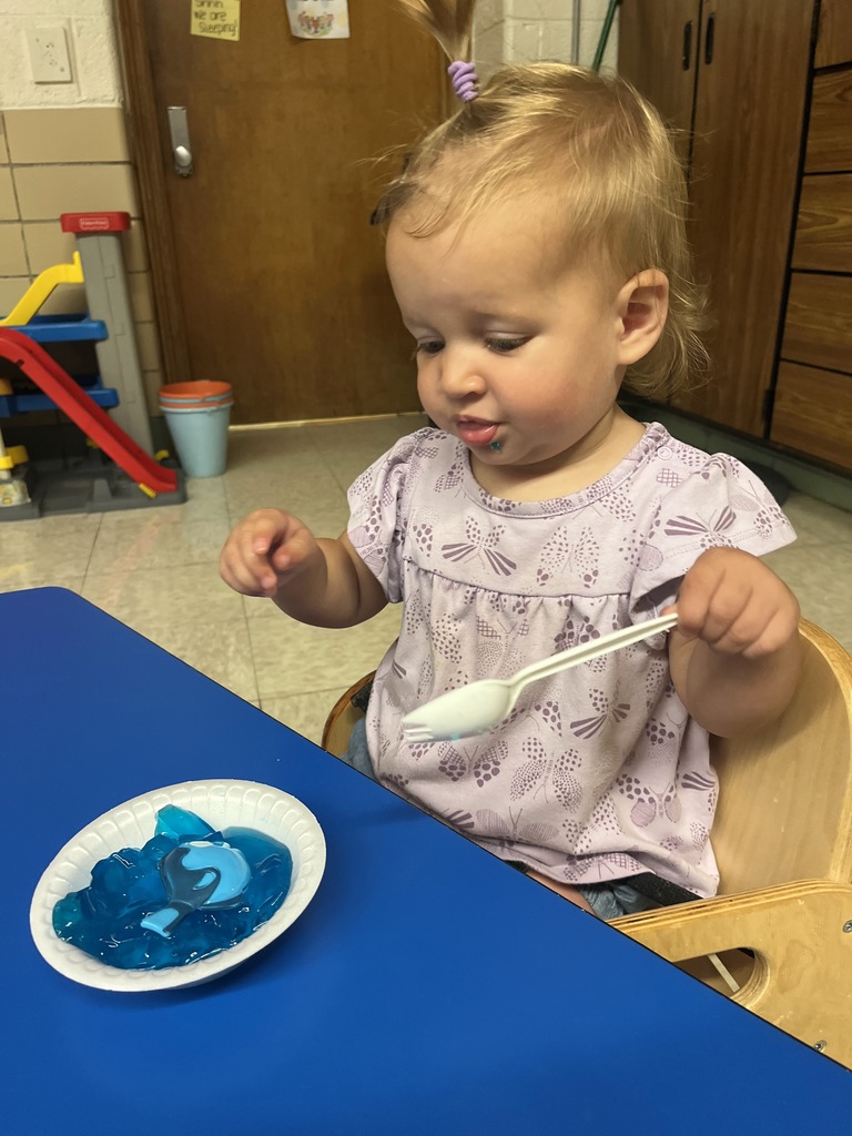 A Toddler eating blue jello with fish toys.