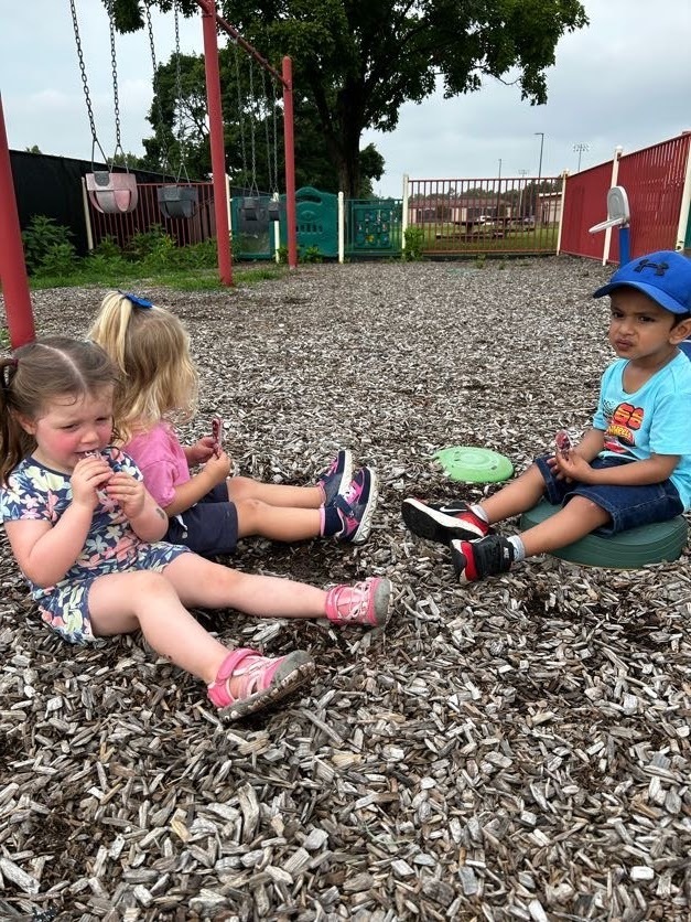 Three kids sitting and having a popsicle. 