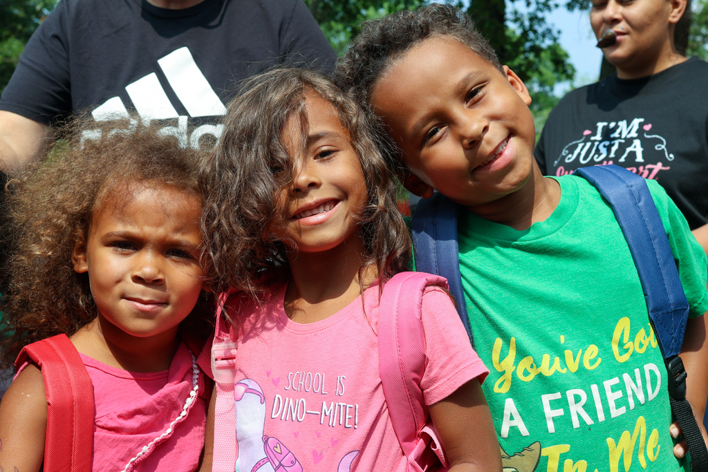 three little kids pose for a photo wearing backpacks