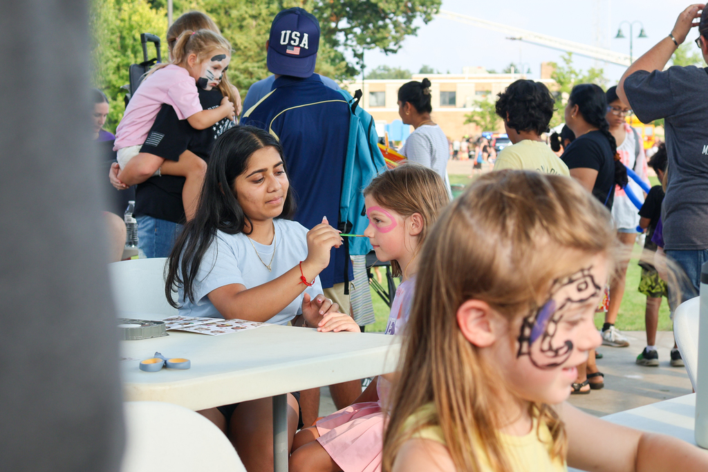 a high school student paints the faces of little kids