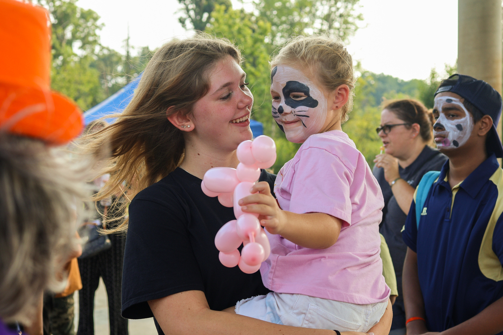 a little girl with face paint and a balloon animal in her mother's arms
