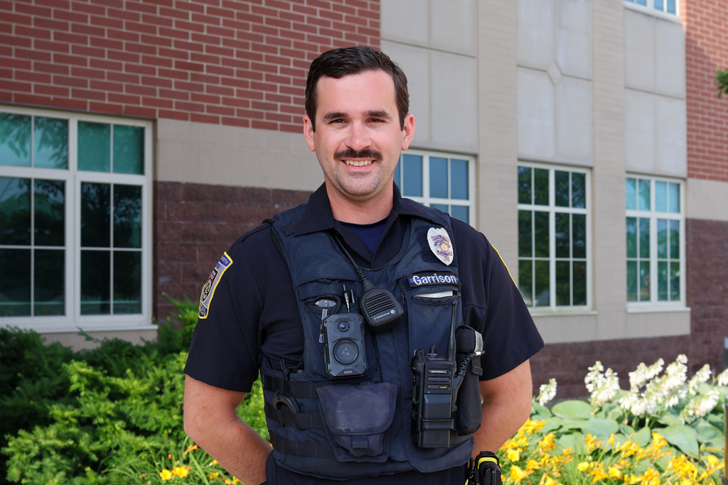 a police officer poses for a photo outside a school building