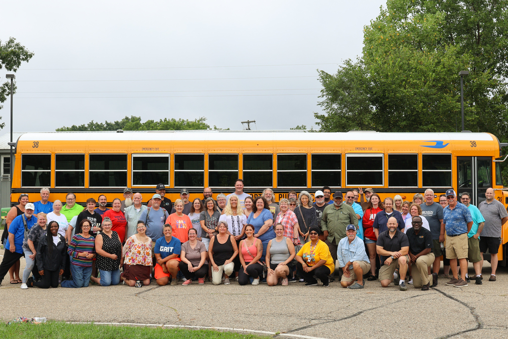 a large group of people pose for a photo in front of a school bus