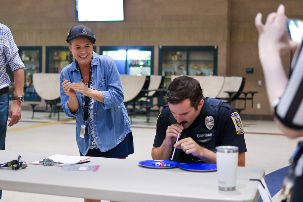 a woman cheers as a man tries to use a straw to move candy from plate to plate