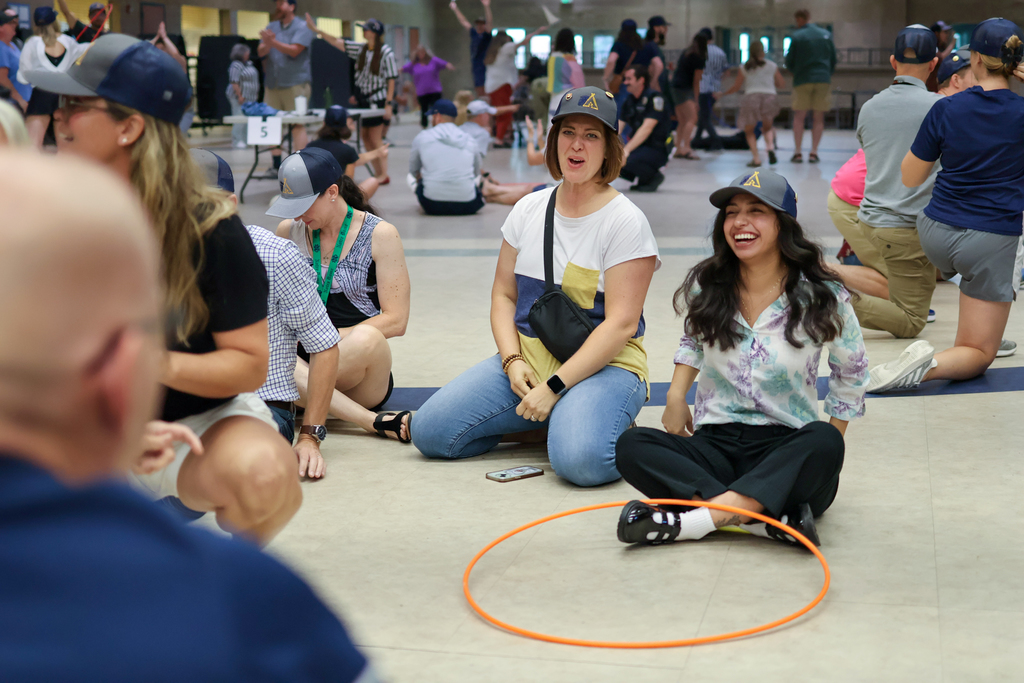 two women laugh sitting on a cafeteria floor