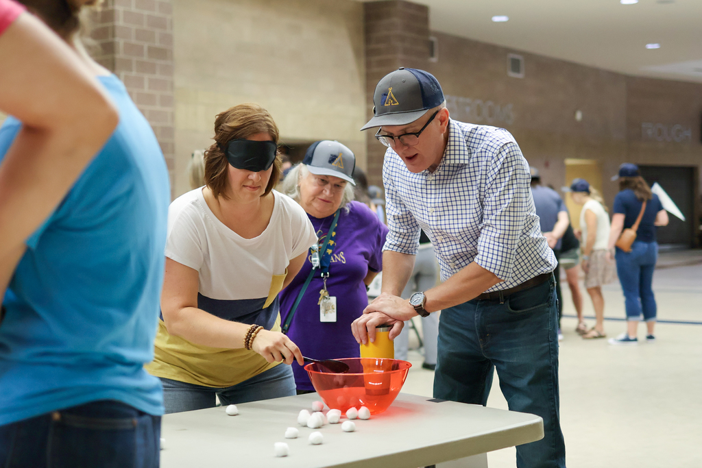 a blind folded woman tries to put cotton balls in a bowl with a spoon