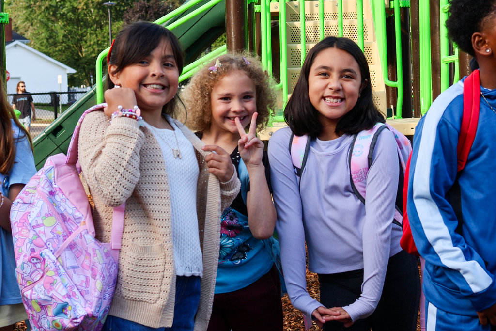 three girls pose for a photo on a school playground