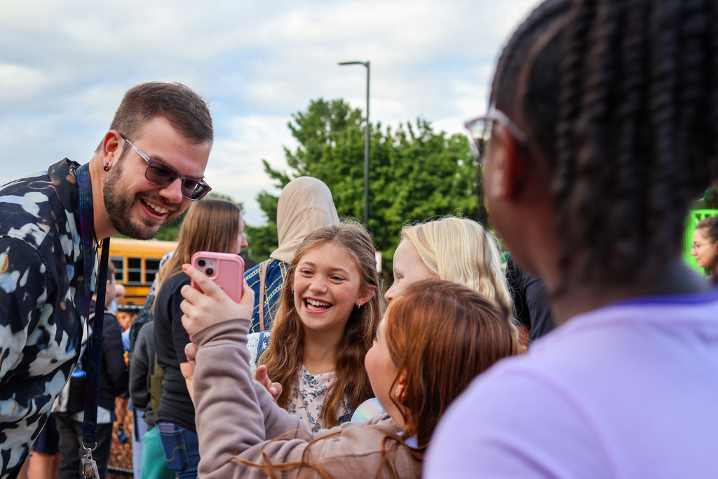 girls smile at a phone standing outside a school
