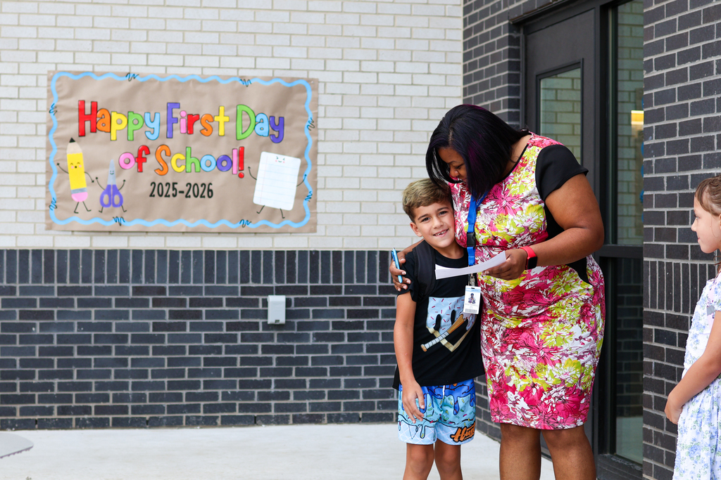 a teacher hugs a student in front of a sign that reads happy first day of school