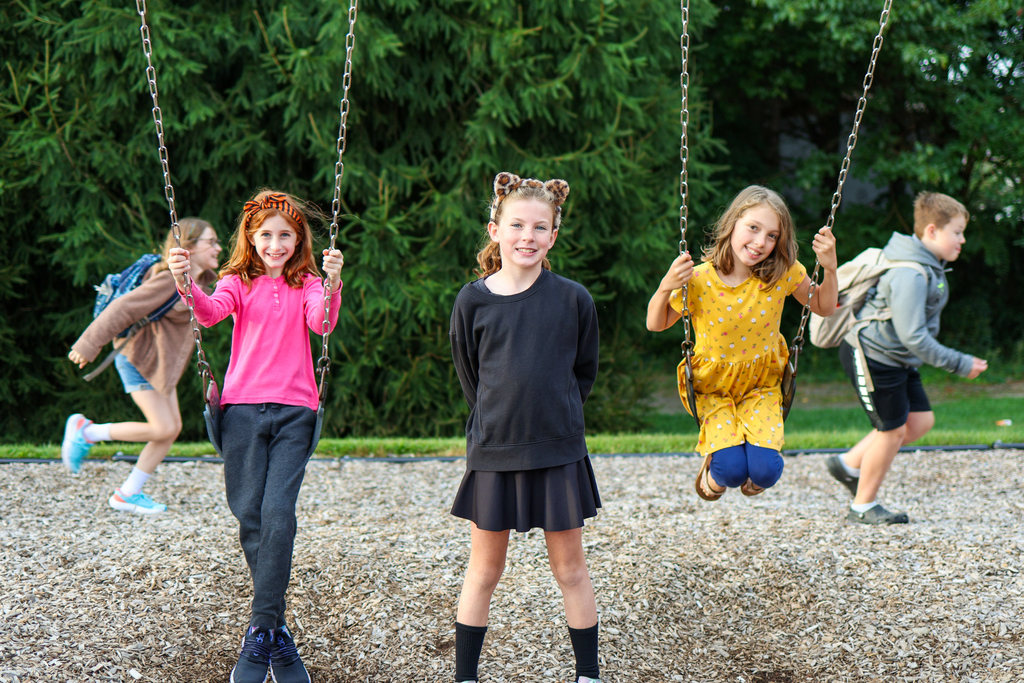 three students pose for a photo on a swingset