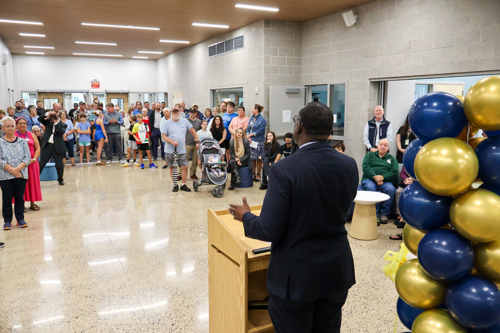 a man speaks at a lectern inside a school 