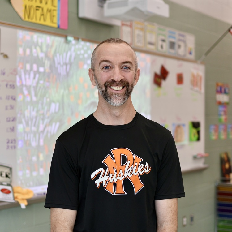 a man poses for a photo inside a classroom 