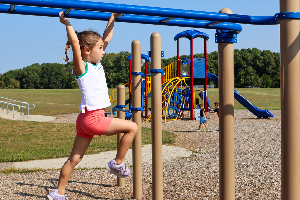 a girl doing the monkey bars outside in a playground