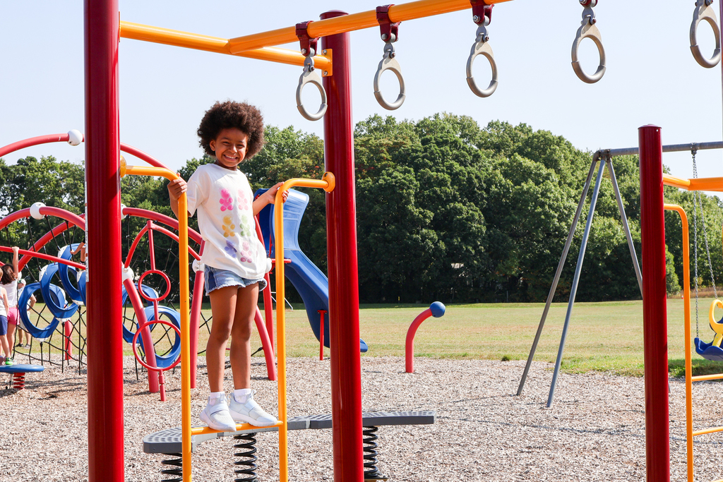 a girl smiles for a photo on playground equipment outside