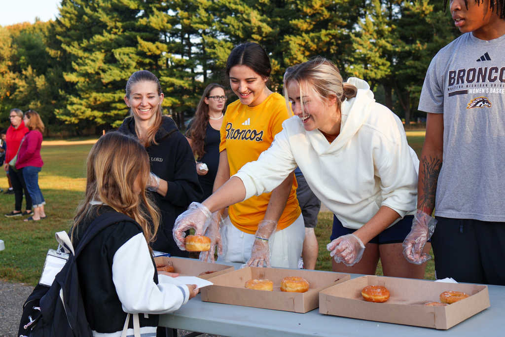 college girls handing out donuts to elementary school students
