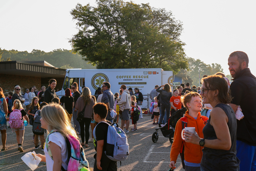 a large group of people gathered outside a school in front of a coffee truck