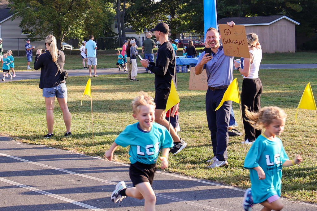 a boy runs by while a dad cheers on the sidelines outside