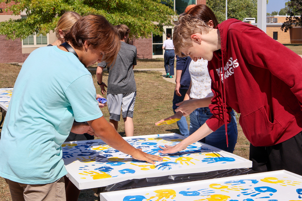 students place their blue and yellow handprints on a white panel