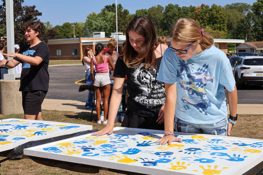two girls leave colorful handprints on a white panel