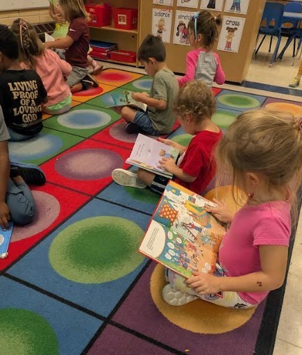 Several students at the carpet together reading a book.