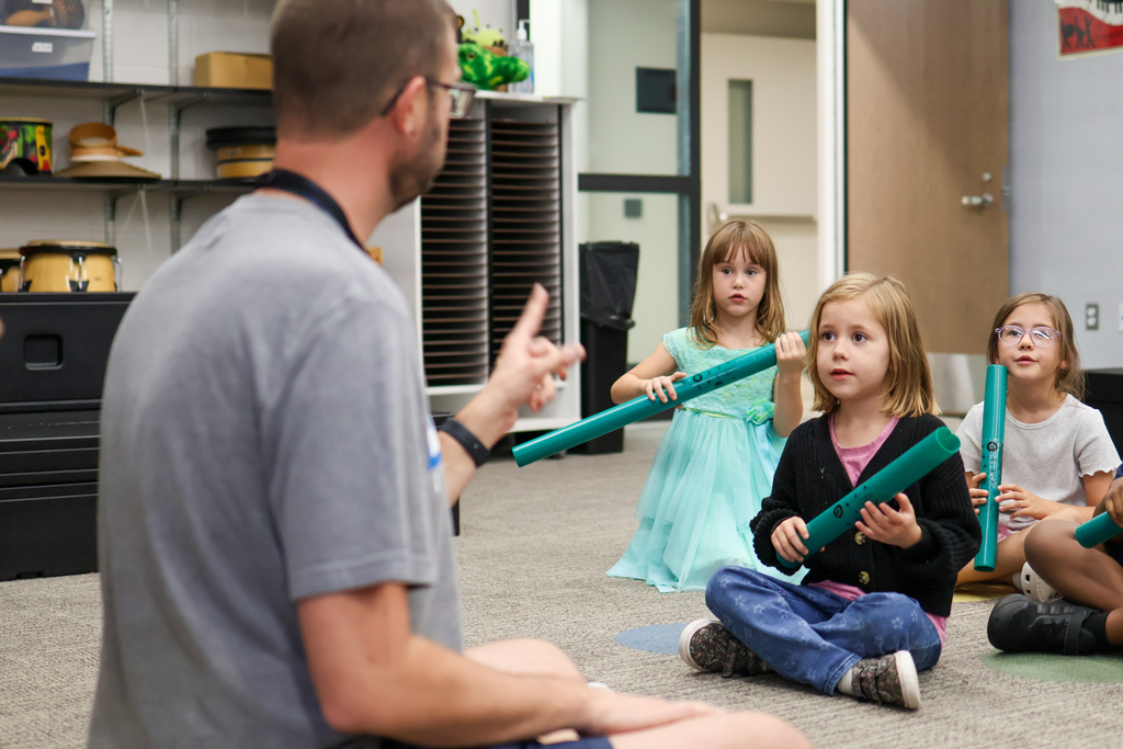 a music teacher instructs students holding instruments in a classroom