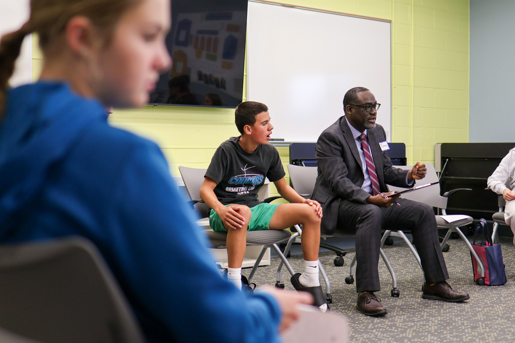 a man speaks to students sitting around a conference room
