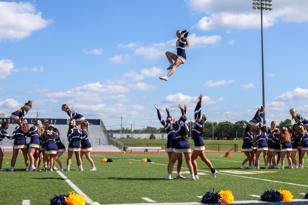 a cheerleader flies through the air during a routine on a football stadium