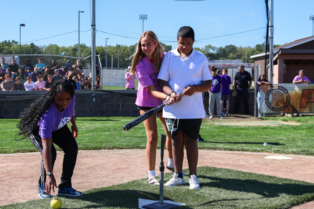 two girls help a boy swing a baseball bat