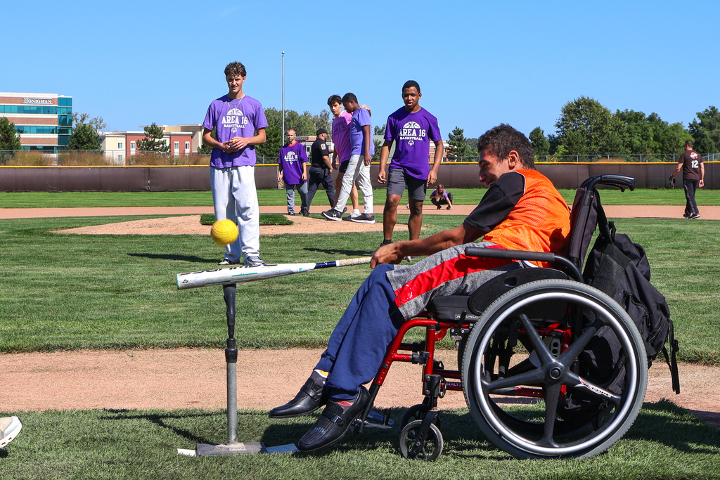 a boy in a wheelchair swings a baseball bat on a field