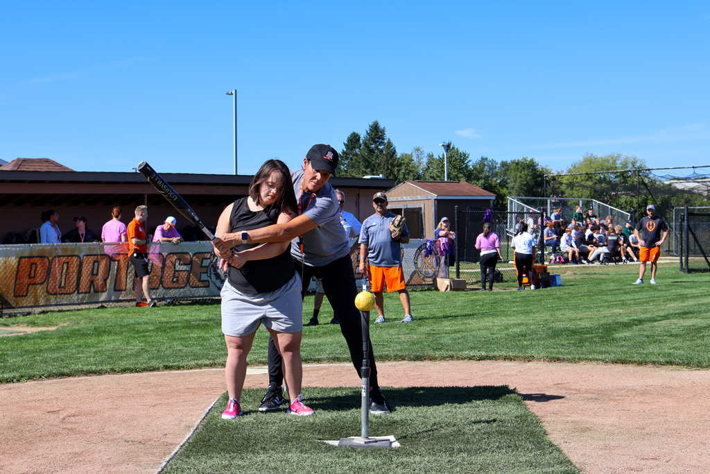 a woman helps a girl swing a baseball bat