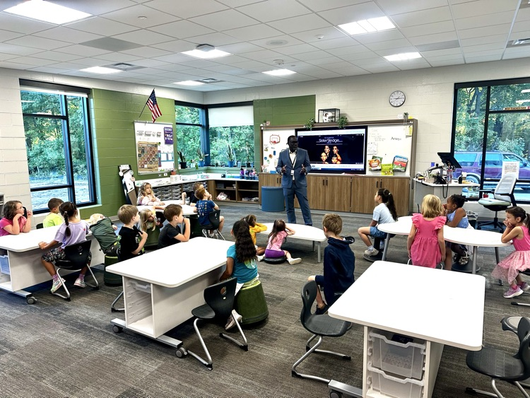 a man speaks to a classroom of young kids