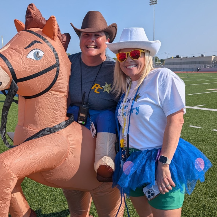 two women wearing cowboy hats pose with an inflatable horse