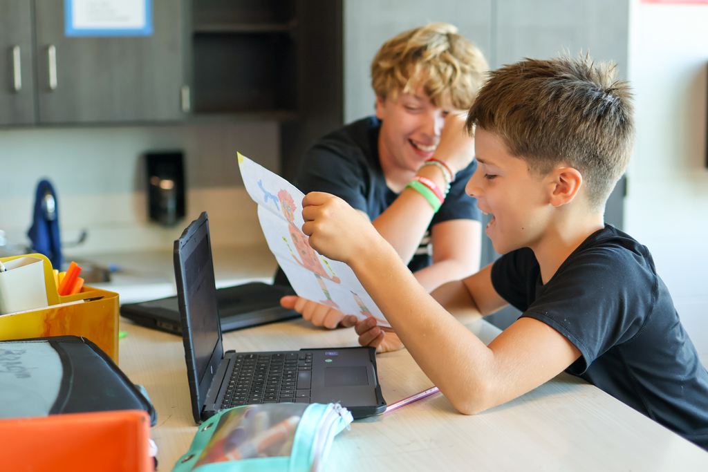 two boys laughing looking at a table in a classroom again