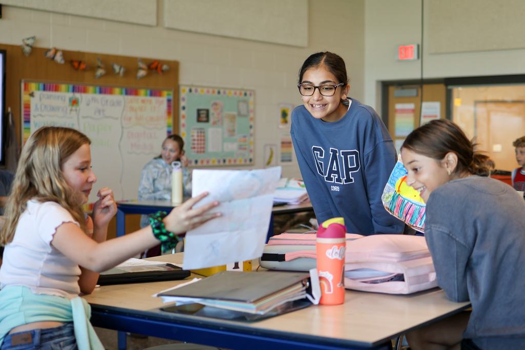 three girls smile looking at a photo together in a classroom